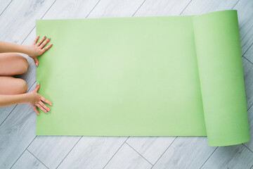 Kids home fitness. Training indoors. Active lifestyle. Health wellbeing. Unrecognizable girl hands on unrolled green yoga mat on light floor with copy space.