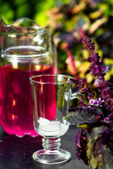 Glass with ice on a dark table with decanter full of purple basil coctail background. Picnic in thу summer garden with trees and leaves.