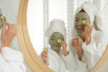 Young mother and her daughter with facial masks near mirror in bathroom