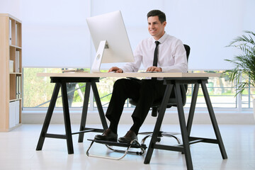 Man using footrest while working on computer in office