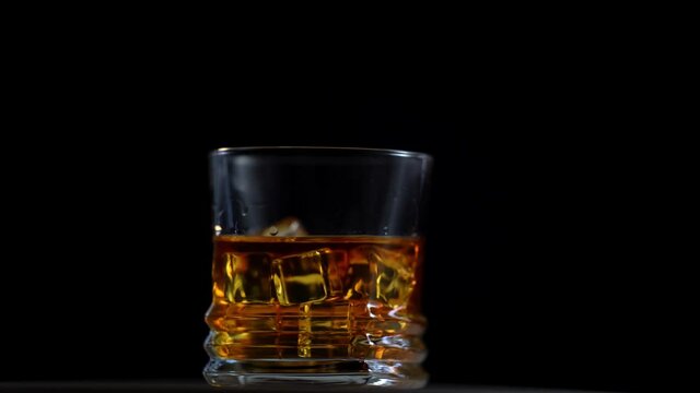 Glass of whiskey with ice cube. Alcohol pouring in the glass from the bottle. Scotch on the rocks. Slider shot. Dark, rustic, background.