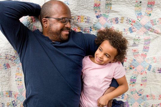 Smiling father and daughter lay on quilt
