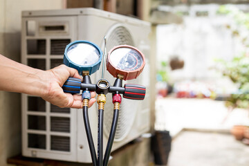 Air repair mechanic using measuring equipment for filling industrial factory air conditioners and...