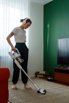 Woman in headphones cleaning floor with wireless vacuum cleaner