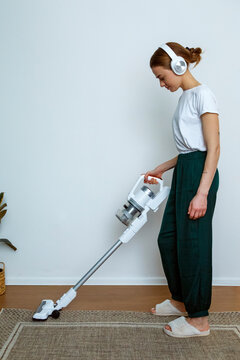Young woman in headphones using modern vacuum cleaner at home