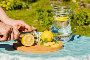 A woman`s hand cuts a lemon to prepare a refreshing drink outdoors on a hot day.