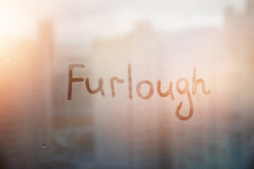 Fototapeta premium Foggy glass on window with written finger word Furlough on muddy sunset glass wet window