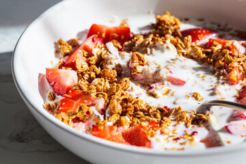 Granola with yogurt and strawberries in white bowl, close-up. Healthy breakfast concept.