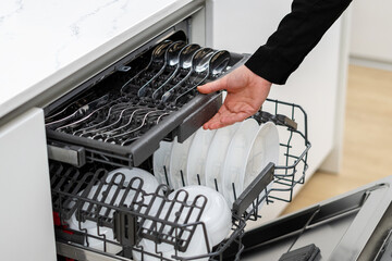 Woman pushing dishwasher drawer with spoons and forks inside