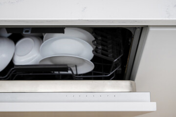 Slightly open dishwasher with utensil and tableware inside