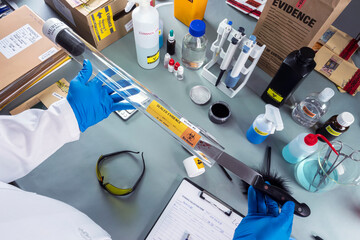 Forensic police remove bloody knife from evidence tube to test suspect's DNA in crime lab,...