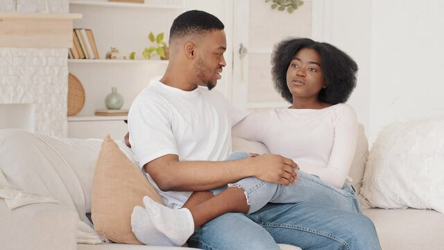 Afro american couple in love newlyweds friends wife and husband african man and ethnic black woman sitting on sofa cuddling girl boyfriend talking chatting dialogue conversation at home indoors