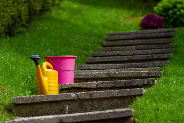 Plastic garden pink watering can stands on freshly plowed ground