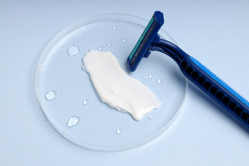 Closeup of smear of shaving cream,razor,water drops on the blue surface