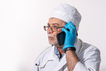 An elderly doctor with a mustache and glasses and conducts a consultation on a mobile phone on a light background.