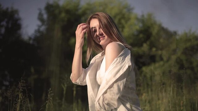 Beautiful Smiling Young Blonde Woman with Clean and pefect Skin relaxing in the park. Happy girl walking in the park. Portrait of cheerful university student looking at camera while adjusting hair