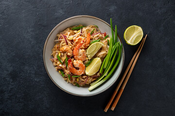Traditional dish Pad Thai with shrimp on a dark stone background, top view