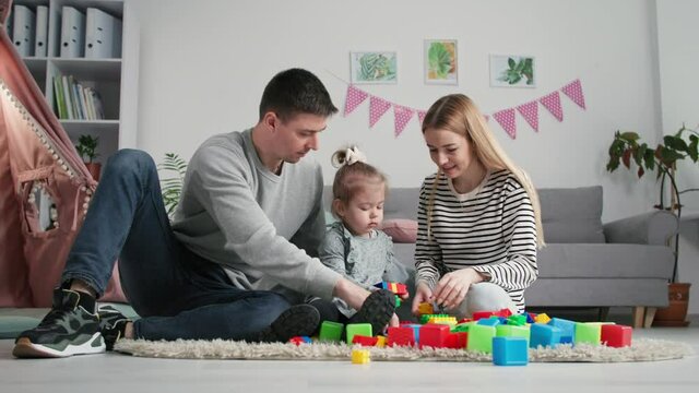 parenting, happy family mom and dad with little daughter play educational games and use eco-friendly color plastic constructor to entertainment kids in children room