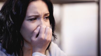 portrait of upset brunette woman crying and covering mouth with hand at home