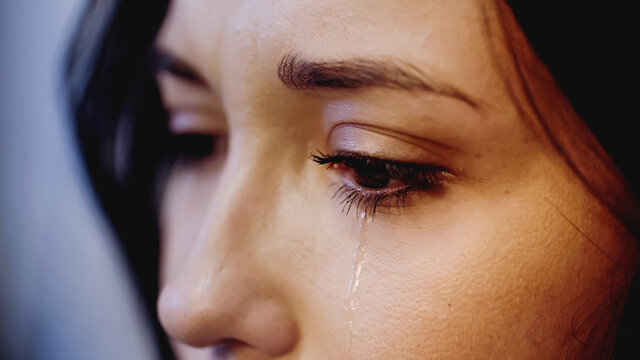 close up view of upset woman crying with tears on face on grey background
