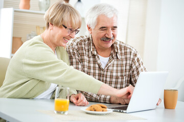 Fototapeta na wymiar Elderly couple talking using laptop having breakfast together