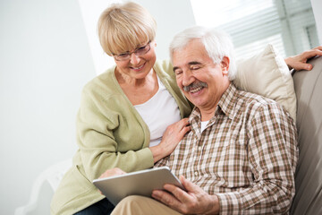 Elderly couple talking using tablet computer together at home