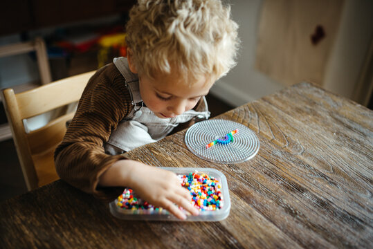 Blond boy crafting with iron beads at a rustic wooden table