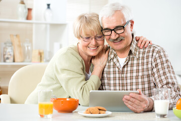 Elderly couple talking using tablet computer having breakfast together