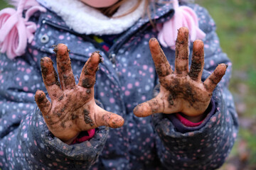 Close-up of the dirty hands of a child girl in warm clothing after playing in mud on a moody winter...