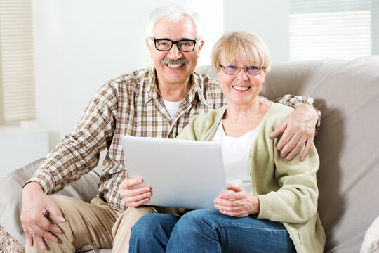Elderly couple talking using laptop together and smiling at camera