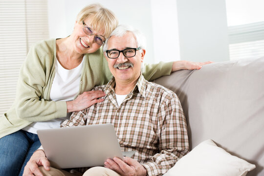 Elderly couple talking using laptop together and smiling at camera