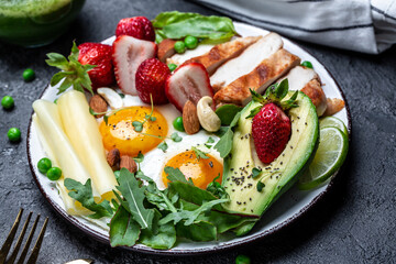 Plate with a keto diet food. Fried egg, avocado, strawberry, grilled chicken fillet, cheese, nuts and arugula. Keto breakfast. Food recipe background. Close up
