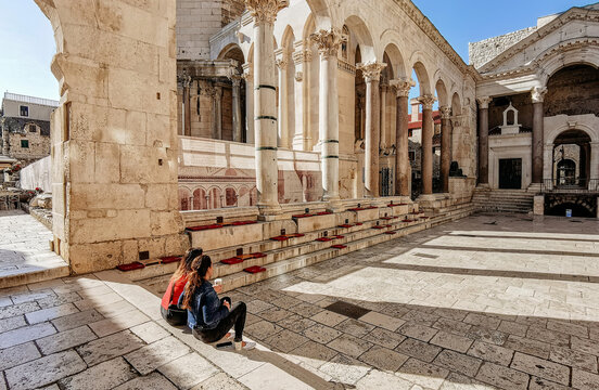 Two women drinking coffee on steps on Peristyle in Diocletian's palace in Split, Croatia.