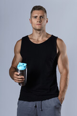 Man wearing blank black tank top is drinking protein or other supplement from a metal shaker