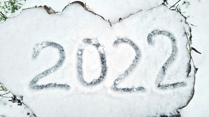 Numbers 2022 are written in the snow on a wooden stump in a winter park. New Year and Christmas background.