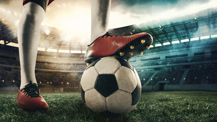 Cropped male soccer, football player standing with ball at the stadium during sport match on light sky background with flashlights.