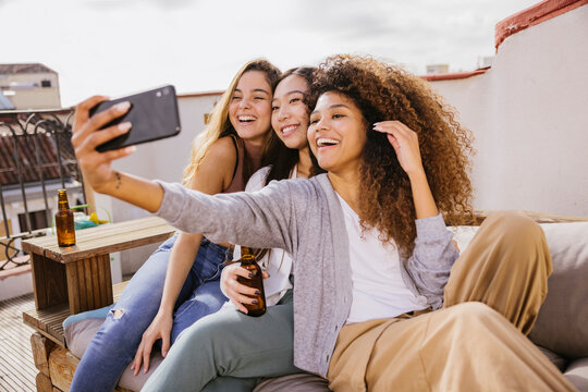 Diverse women relaxing on terrace and browsing smartphone together