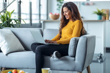 Obraz premium Pretty young woman working with her laptop while sitting on couch at home.