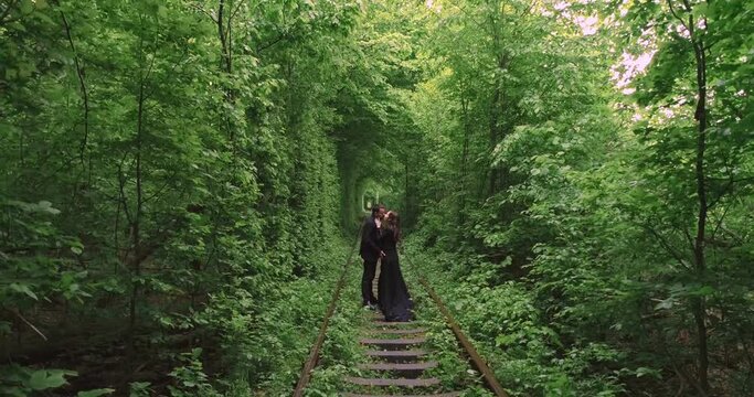 Happy beautiful girl pregnant with her husband outdoors. A walk in the woods. A railway in the summer forest. Tunnel of Love, green trees and the railroad