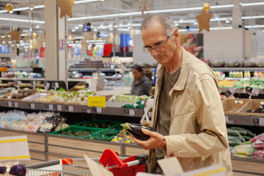senior man in grocery store choosing vegetables, food shopping in supermarket