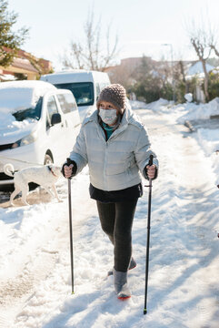 Elderly woman using ski poles to help her walk on the snow in the street