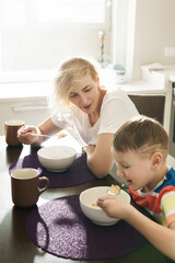 Obraz na płótnie Canvas Beautiful mother and her cute son eating healthy cornflakes for breakfast