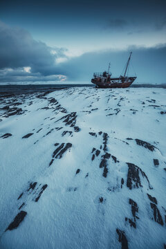 Gloomy landscape with an old abandoned ship on the snow-covered coast of the north sea
