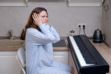 A sad woman experiences sitting at an electric piano in a home kitchen