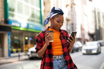 Young african woman using the phone while drinking cofee. Beautiful woman drinking coffee outdoors