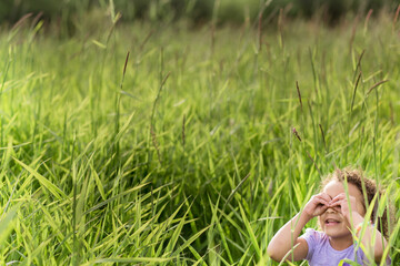 Girl peers through hands in field of tall grass