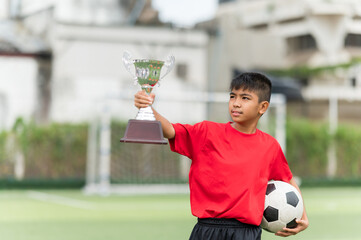 Asian Teenage soccer player holding a silver color trophy and a football
