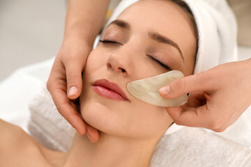 Young woman receiving facial massage with gua sha tool in beauty salon, closeup
