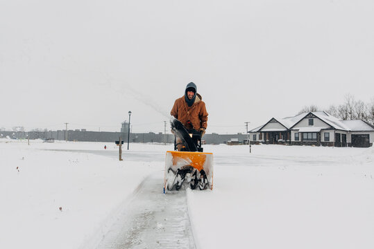 Clearing snowy driveway with a snowblower. 