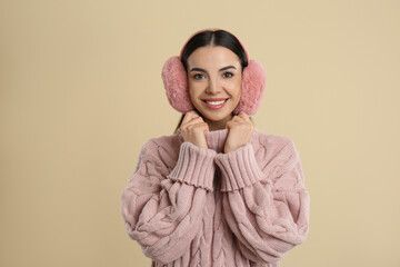 Beautiful young woman wearing earmuffs on beige background